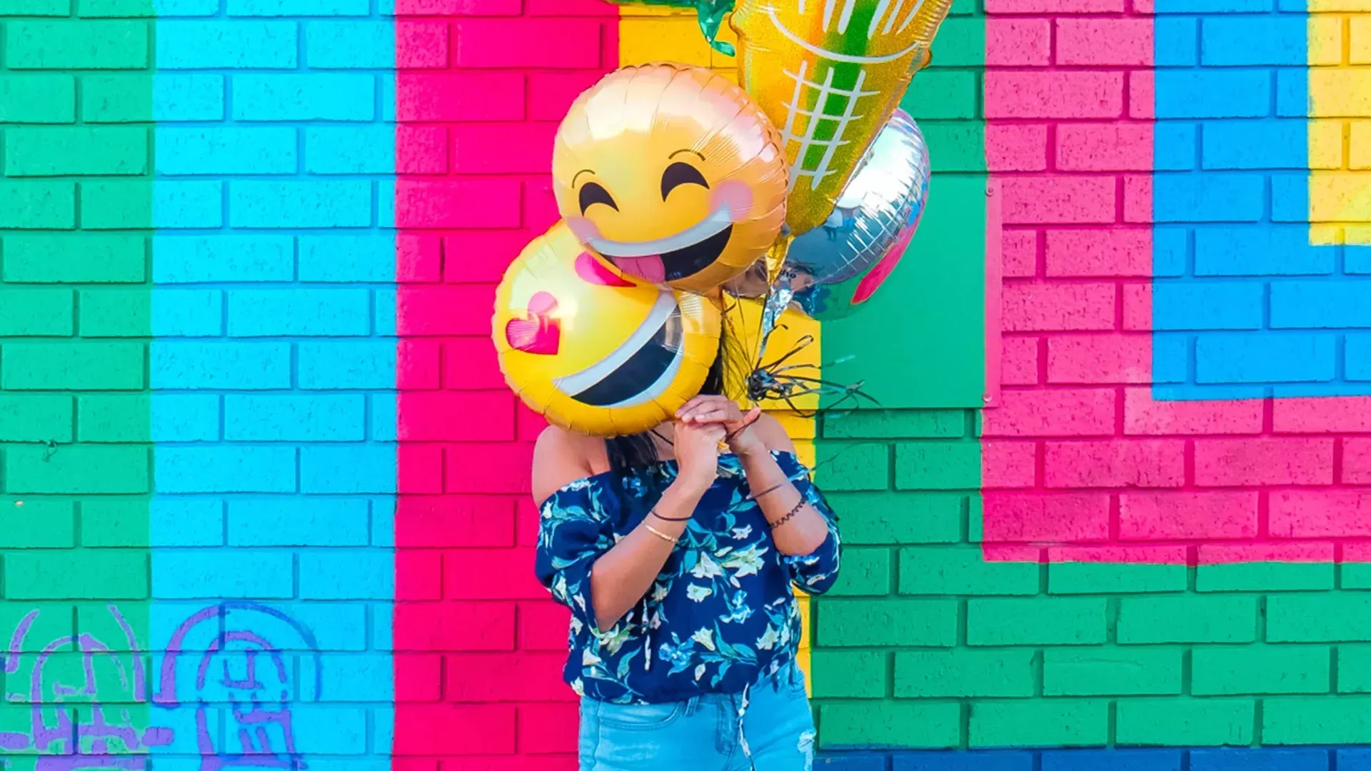 Une fille fête son anniversaire avec des ballons devant une fresque colorée.