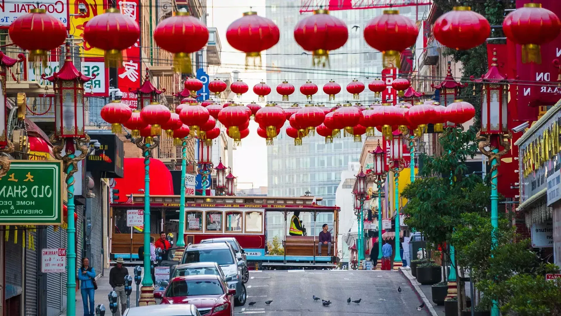 Une rue vallonnée du quartier chinois de San Francisco est représentée avec des lanternes rouges suspendues et un tramway qui passe.